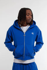 Mannequin homme portant un hoodie zippé et jogging bleu électrique Cynique en coton 450 GSM. Coupe oversize, logo brodé blanc côté cœur, style streetwear minimaliste.