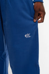 Gros plan sur le logo brodé blanc du jogging bleu Cynique, positionné sur la cuisse droite. Matière coton épais 450 GSM, coupe oversize. Détail texture et finition premium.