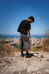 Jort gris Cynique porté en extérieur. Broderie logo au dos, coupe large. Short en jean brut et minimaliste, pensé pour durer, taillé pour le réel.