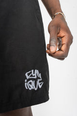 Détail du logo Cynique brodé sur le maillot de bain noir. Short minimaliste, brut, streetwear. Focus sur la finition et l’attitude.