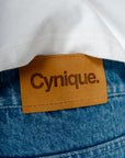 Détail patch cuir Cynique sur le Jort bleu. Short en jean brut, solide. Signature minimaliste et assumée, taillée pour durer.