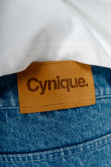 Détail patch cuir Cynique sur le Jort bleu. Short en jean brut, solide. Signature minimaliste et assumée, taillée pour durer.