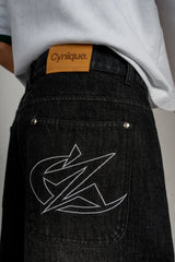 Zoom sur le jort noir Cynique. Logo brodé et patch cuir signature. Denim épais et brut, conçu pour durer.