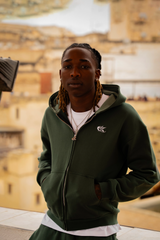 Hoodie Cynique vert porté, ambiance ocre de la médina. Coupe large, broderie blanche discrète, pièce essentielle pour un style streetwear premium et décontracté.