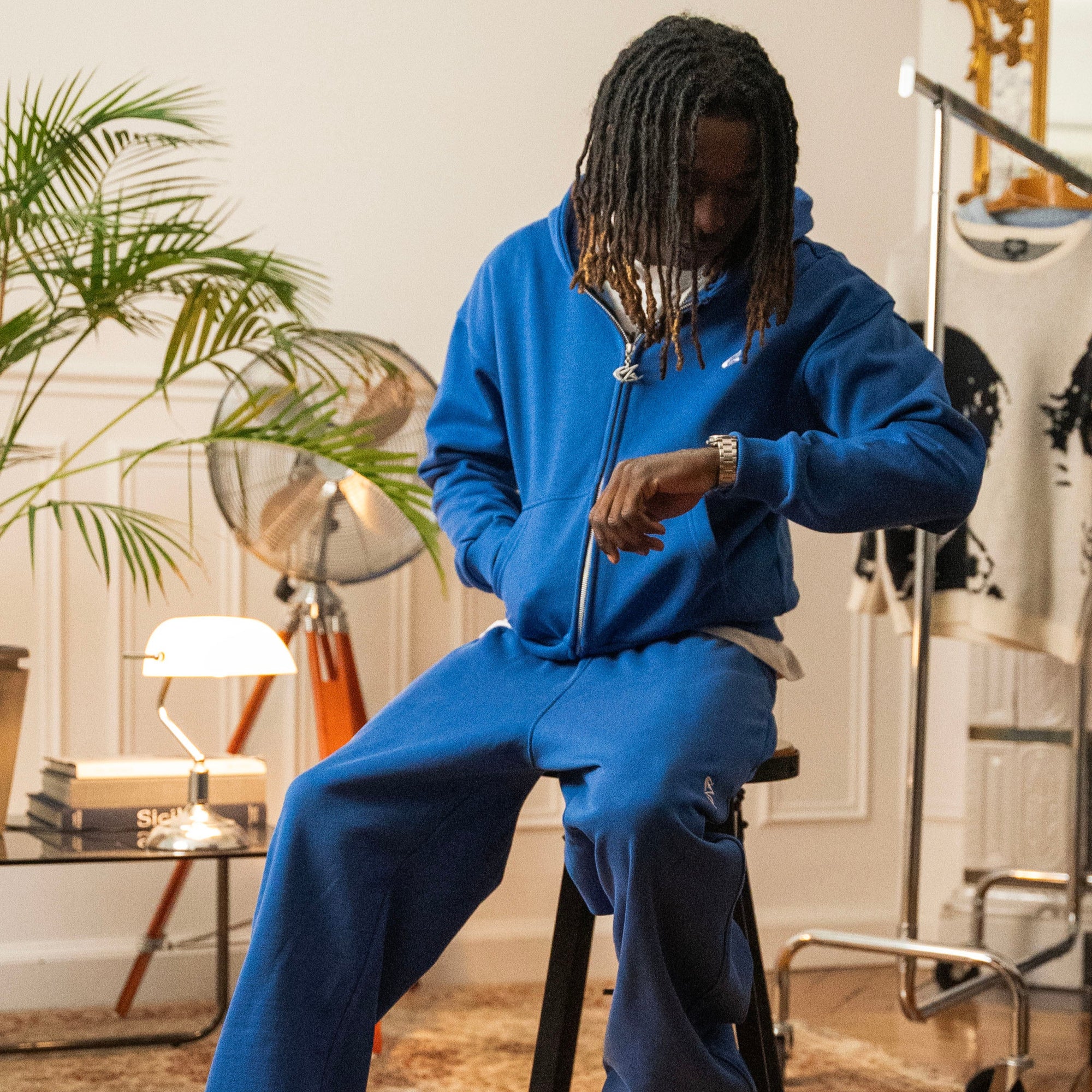 Cynique tracksuit worn by male model — bold blue zip-up hoodie and matching joggers styled indoors with ‘Tracksuits’ call-to-action text overlay