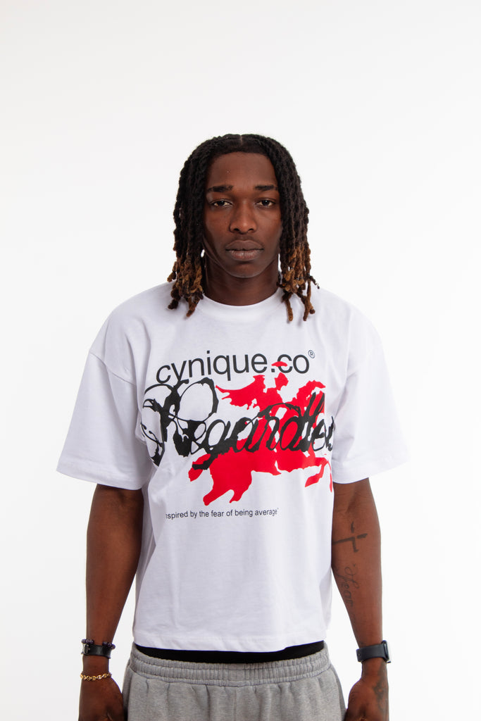 Male model wearing Cynique Regardless Tee — white oversized T-shirt with red horse graphic and bold ‘Regardless’ text, styled with gray sweatpants in studio
