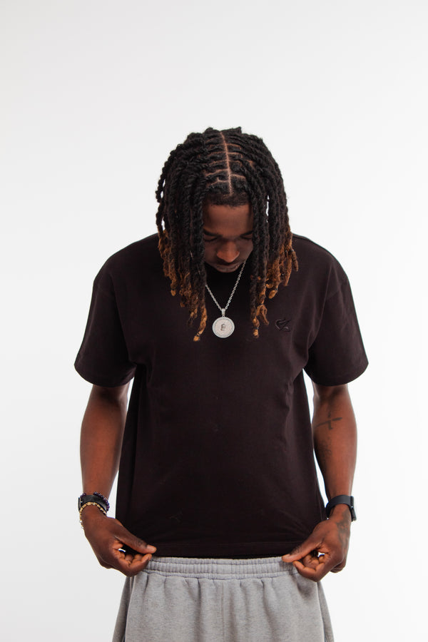 Model wearing Cynique Vanta Black Tee — boxy fit heavyweight T-shirt in 100% cotton with subtle chest logo, styled casually with gray sweatpants