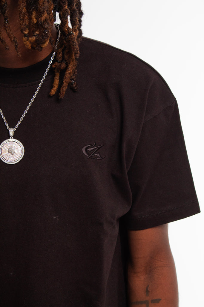 Chest detail of Cynique Vanta Black Tee — tonal embroidered logo on heavyweight cotton fabric, styled with chain pendant necklace in a studio setting