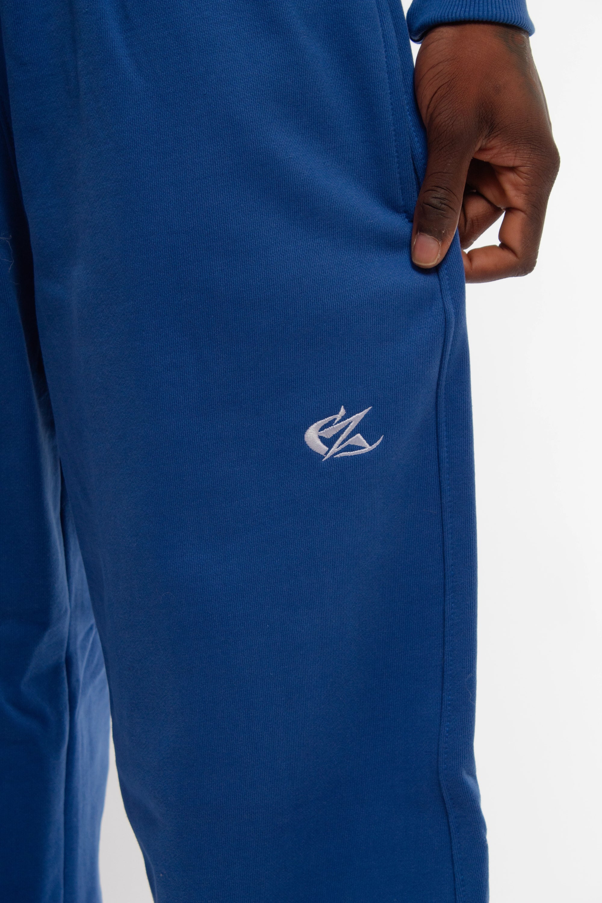 Gros plan sur le logo brodé blanc du jogging bleu Cynique, positionné sur la cuisse droite. Matière coton épais 450 GSM, coupe oversize. Détail texture et finition premium.