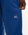 Gros plan sur le logo brodé blanc du jogging bleu Cynique, positionné sur la cuisse droite. Matière coton épais 450 GSM, coupe oversize. Détail texture et finition premium.