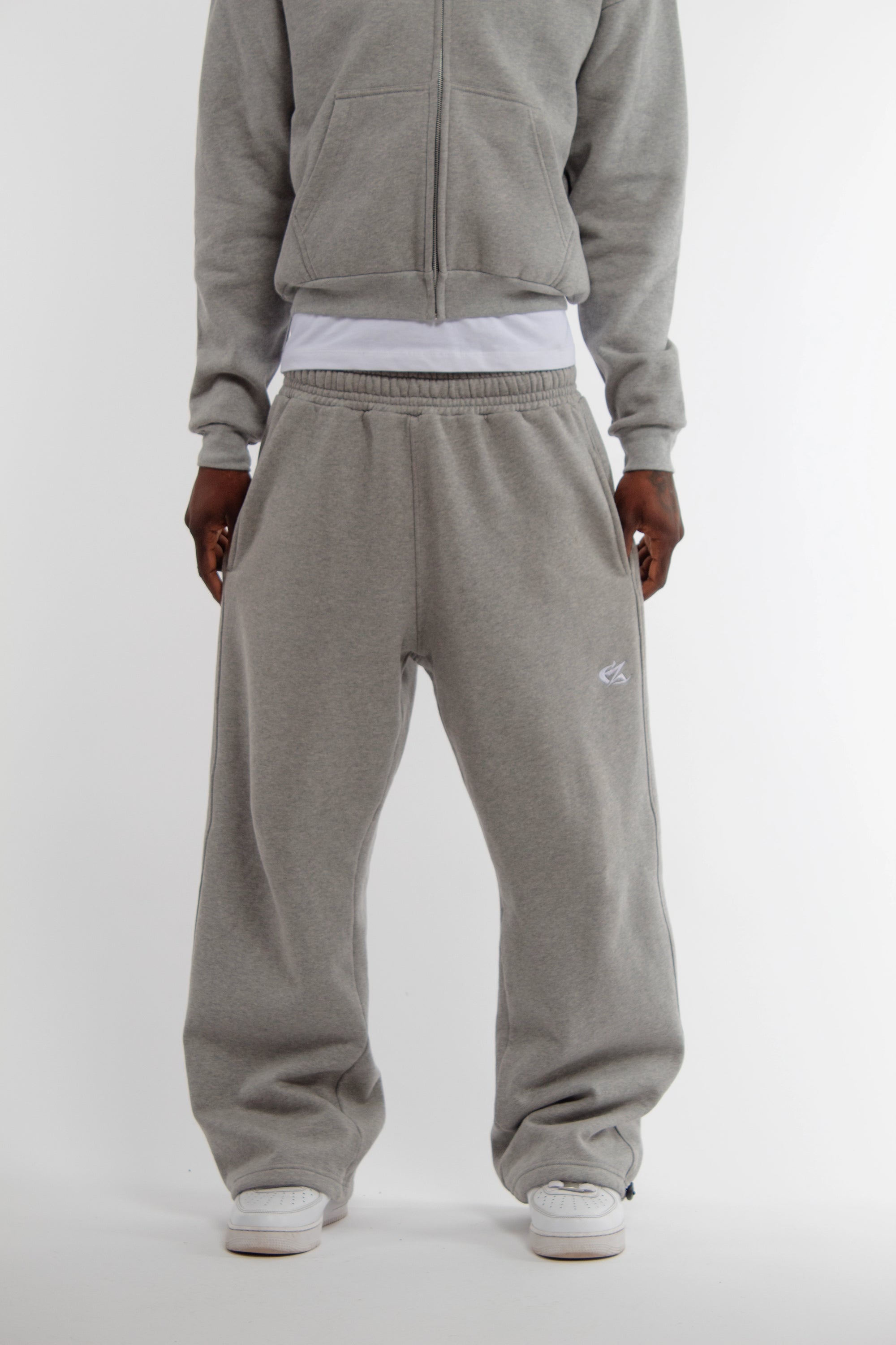 Vue arrière d’un mannequin portant un ensemble hoodie zippé et jogging gris Cynique. Coton 450 GSM, coupe oversize unisexe, poche plaquée arrière, ambiance intérieure stylée.