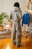 Model wearing Cynique Basic Gray tracksuit from behind — oversized hoodie and joggers in cotton with rear pocket logo, styled in cozy indoor setting