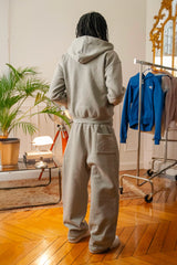 Vue arrière d’un mannequin portant un ensemble hoodie zippé et jogging gris Cynique. Coton 450 GSM, coupe oversize unisexe, poche plaquée arrière, ambiance intérieure stylée.
