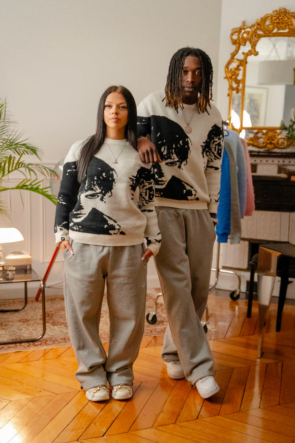 Male and female models wearing Cynique Monarch Knit sweaters — black and white portrait crewnecks styled with oversized joggers and sneakers in cozy indoor setting