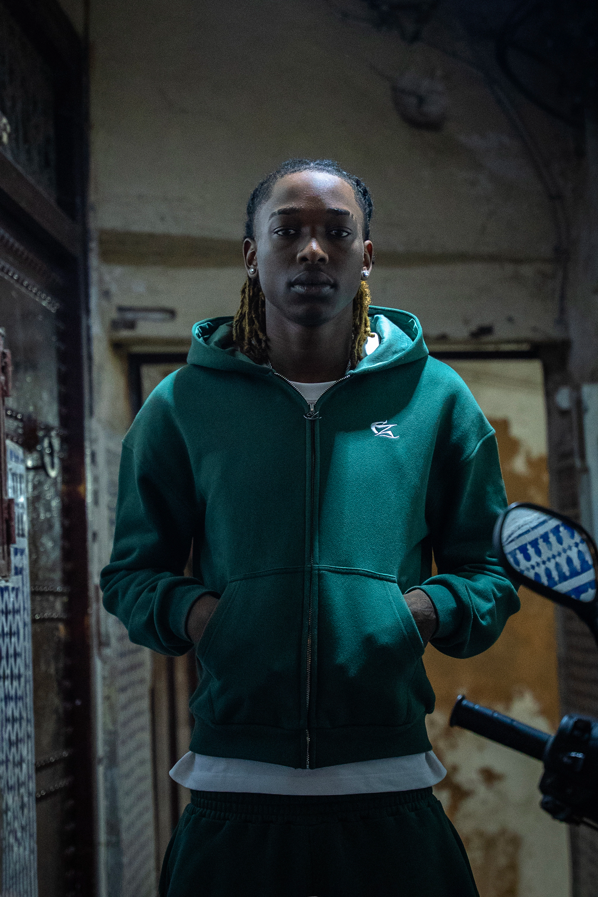 Hoodie Cynique vert porté, ambiance urbaine sombre. Coupe oversized, broderie signature ton sur ton, parfait pour un look street discret et travaillé.