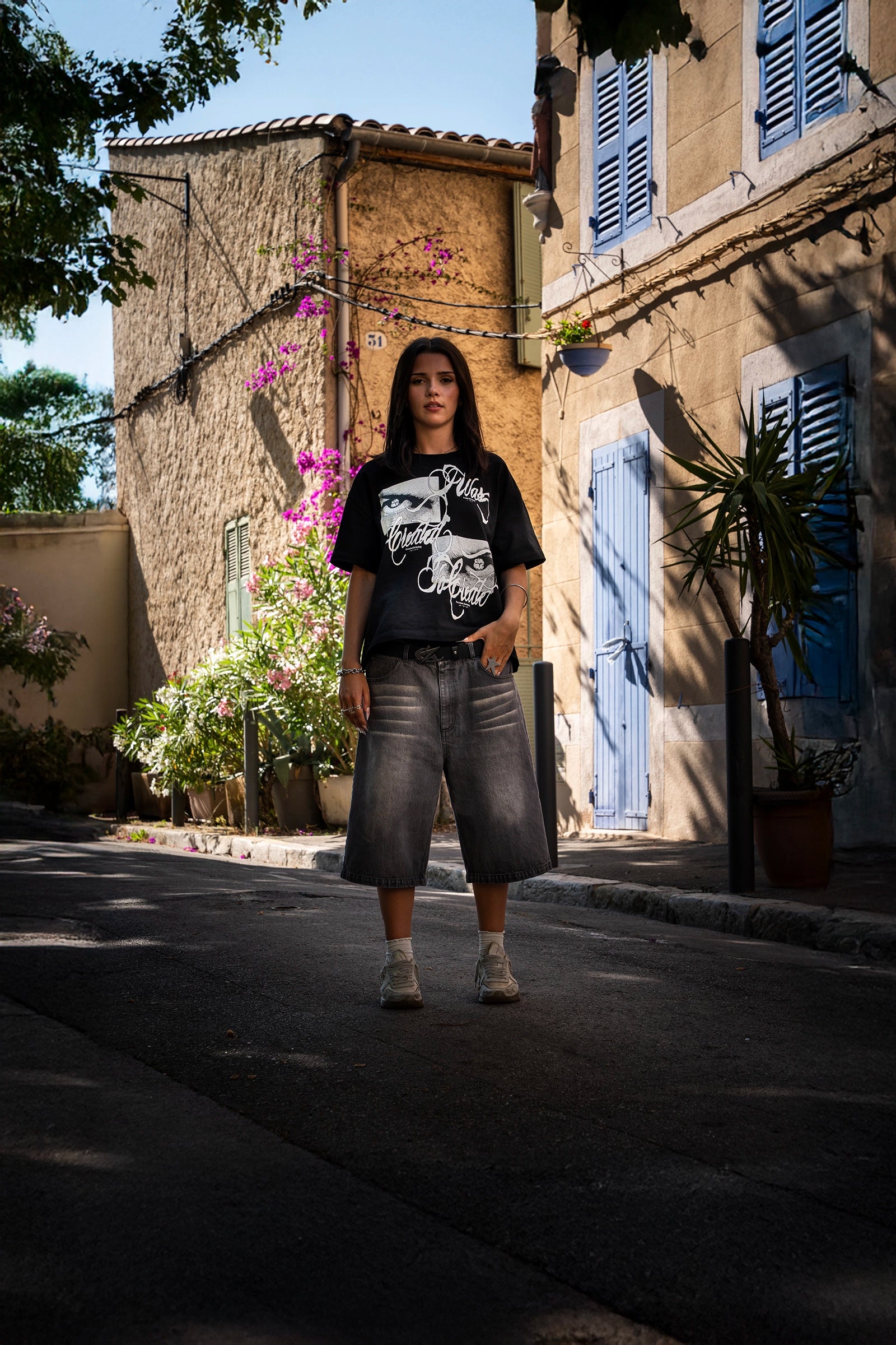 Look streetwear Cynique en extérieur. Jort gris en denim, t-shirt Created. Coupe large, style brut, minimaliste, pensé pour le réel.