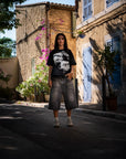 Look streetwear Cynique en extérieur. Jort gris en denim, t-shirt Created. Coupe large, style brut, minimaliste, pensé pour le réel.