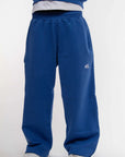 Jogging bleu électrique Cynique en coton épais 450 GSM, coupe oversize avec cordons de serrage aux chevilles. Logo brodé blanc sur la cuisse droite. Porté avec sneakers blanches.