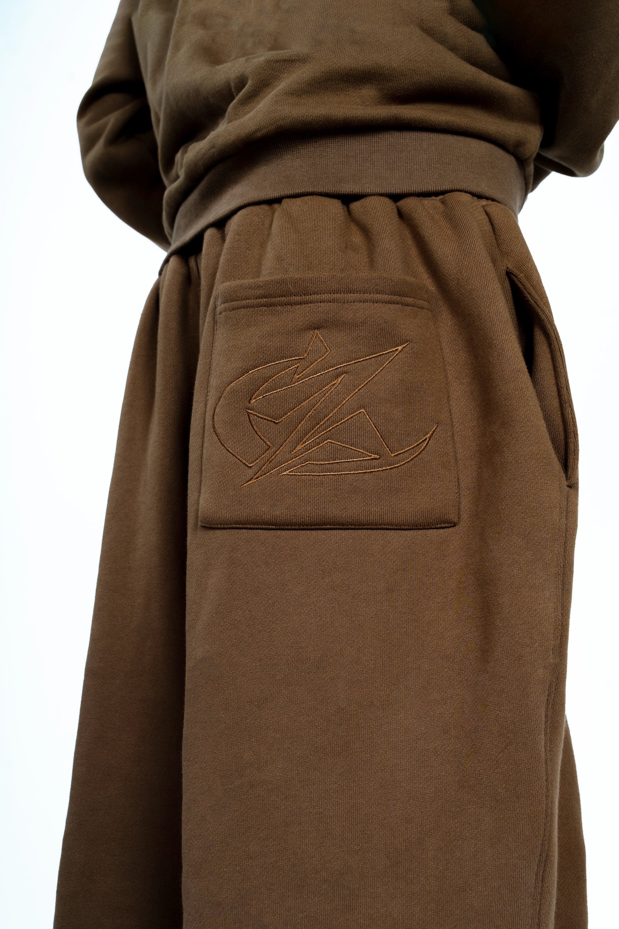 Détail du pantalon large marron Cynique. Broderie ton sur ton du logo iconique sur la poche arrière pour un look minimaliste et travaillé.