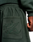 Détail broderie du jogging vert Cynique. Une finition soignée et un logo ton sur ton pour un look minimaliste et affirmé.