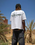 Vue arrière du t-shirt Cynique Maroc porté dans le désert. Lettrage arabe et slogan “damn all to crown.” Style affirmé et influence nord-africaine forte.