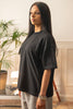 Female model wearing Cynique Vanta Black Tee — oversized unisex T-shirt in 100% cotton with tonal chest logo, styled with gray sweatpants in a relaxed indoor setting