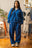 Femme debout portant un ensemble streetwear Cynique composé d’un hoodie zippé et d’un jogging bleu électrique. Coton 450 GSM, coupe oversize, logos brodés blancs. Look unisexe dans un décor intérieur stylé.
