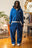 Mannequin homme portant un ensemble Cynique composé d’un hoodie zippé et d’un jogging bleu électrique. Coton 450 GSM, coupe oversize, logos brodés blancs, style streetwear dans un décor intérieur rétro.