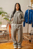 Female model wearing Cynique Basic Gray tracksuit — boxy zip-up hoodie and oversized joggers in soft cotton, styled with statement sneakers in a modern interior