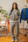 Femme debout portant un ensemble hoodie zippé et jogging gris Cynique. Coupe oversize unisexe, coton 450 GSM, logo brodé blanc, style streetwear épuré dans un intérieur vintage.