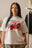 T-shirt blanc Cynique porté par une femme. Design streetwear avec visuel “Regardless” noir et rouge imprimé sur la poitrine, slogan “inspired by the fear of being average”. Coupe oversize unisexe, coton 210 GSM. Look urbain et affirmé.