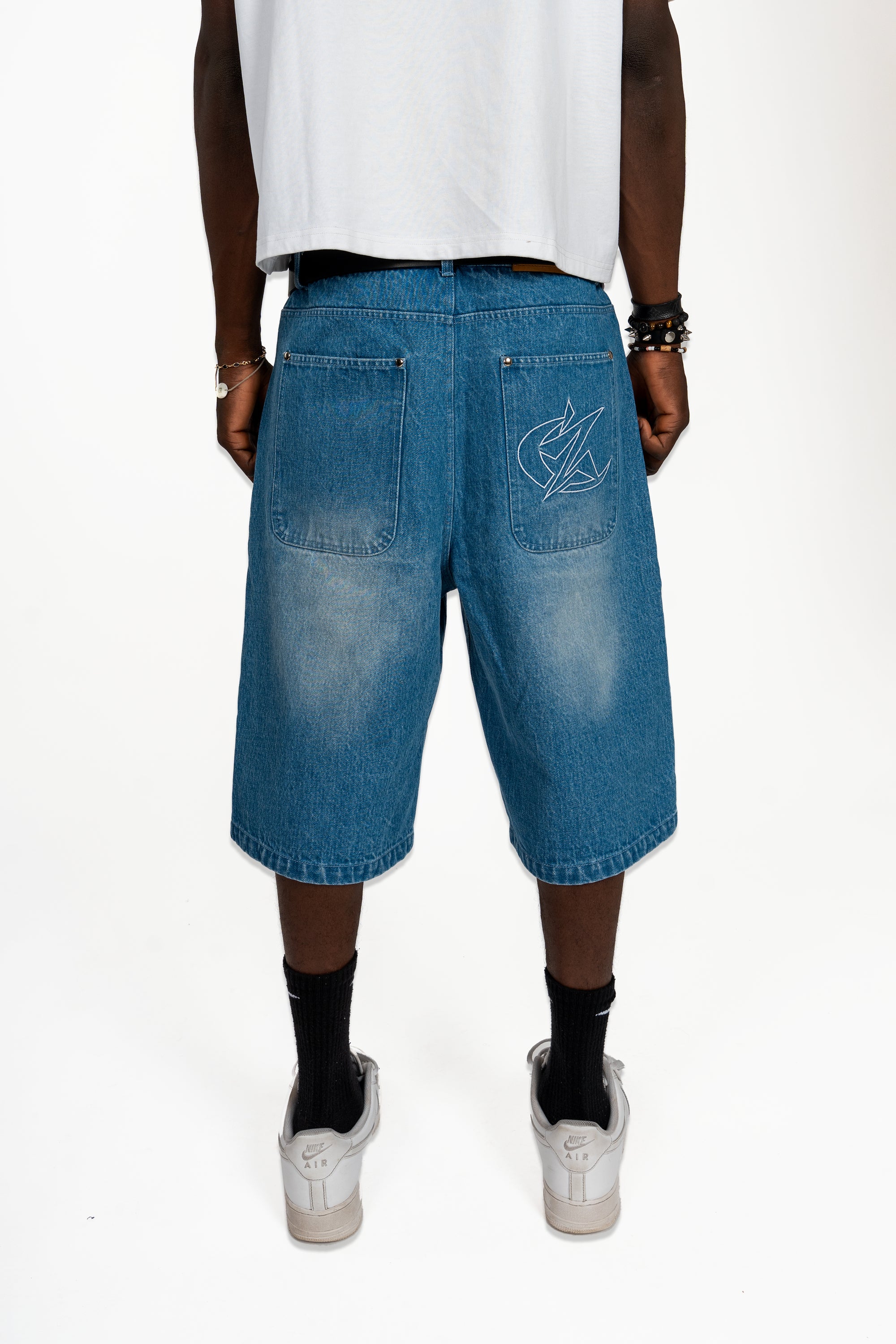 Jort bleu Cynique en denim porté. Broderie logo arrière, coupe large. Short en jean brut et solide, style minimaliste, taillé pour durer.