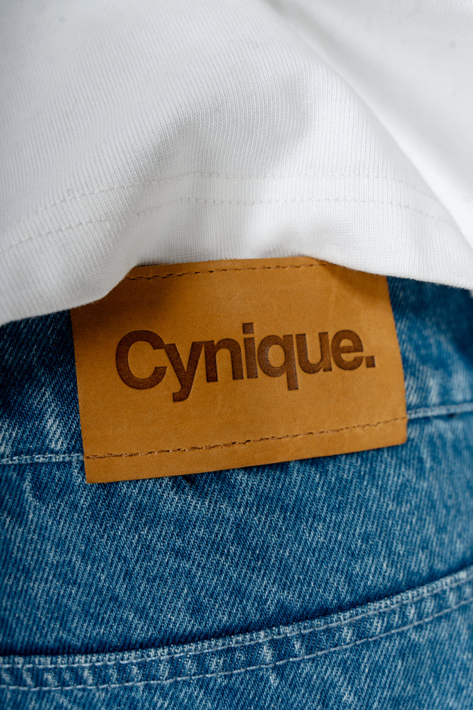 Détail patch cuir Cynique sur le Jort bleu. Short en jean brut, solide. Signature minimaliste et assumée, taillée pour durer.