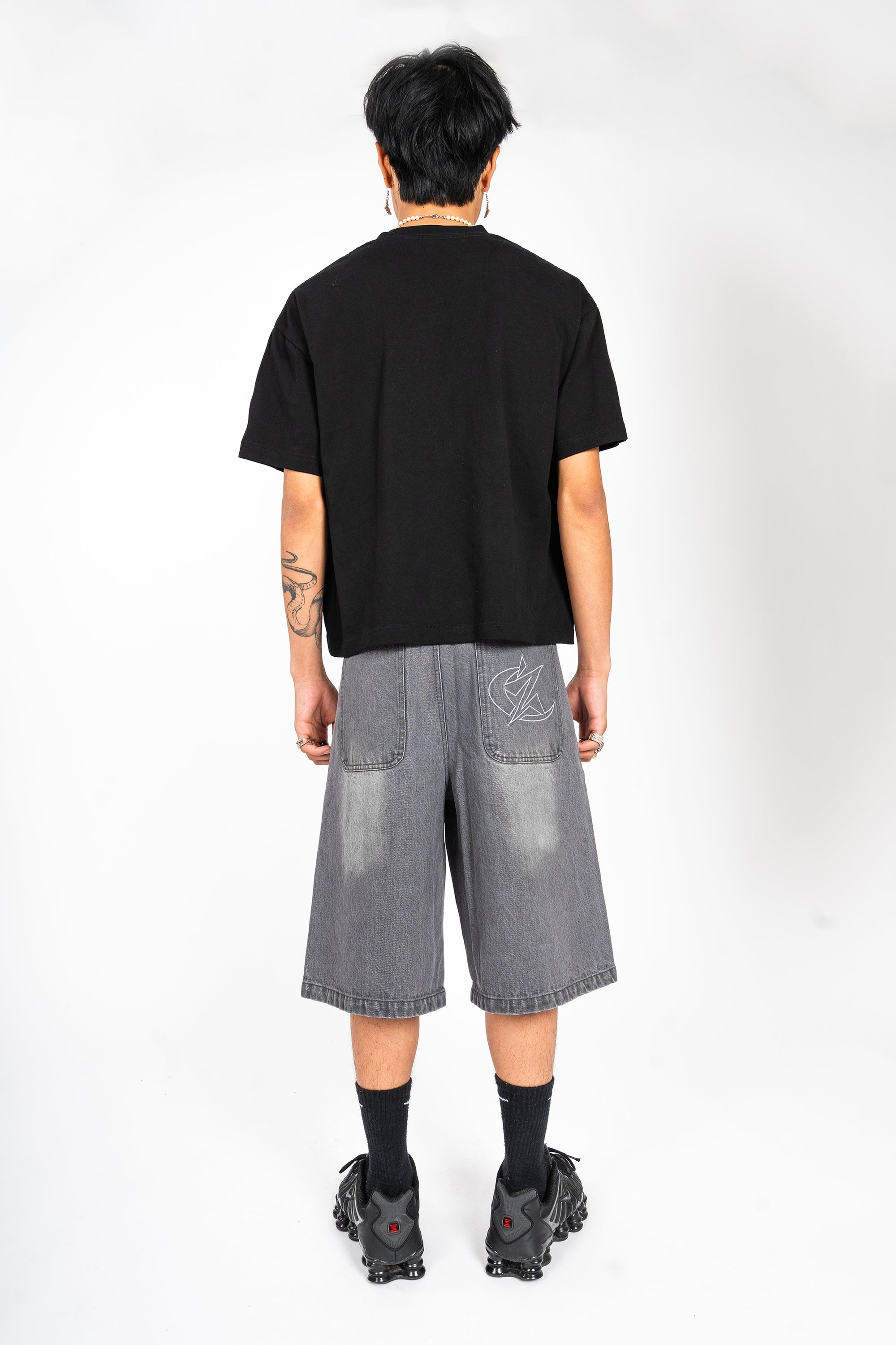 Jort gris Cynique en denim vu de dos. Broderie logo arrière, coupe large. Short en jean brut et solide, taillé pour durer, style minimaliste.