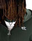 Zoom sur le hoodie Cynique vert sapin, détails soignés : broderie blanche discrète et curseur de fermeture éclaire customisé. Pièce minimaliste mais travaillée, à l’image du streetwear Cynique.